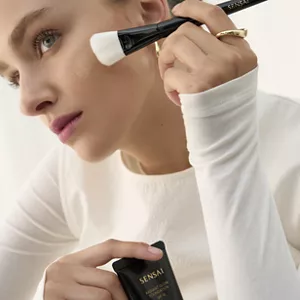 Person applying Radiant Glow Foundation on their face with the Foundation Brush while holding bottle in other hand